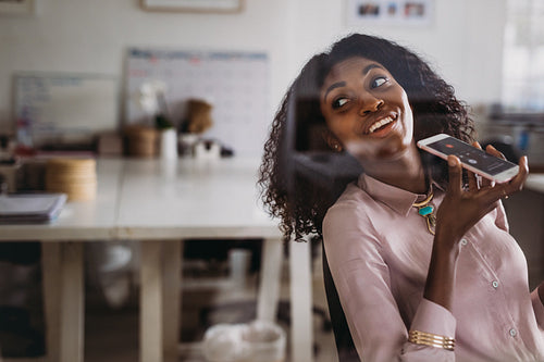 Businesswoman talking over mobile phone on loudspeaker while working at home