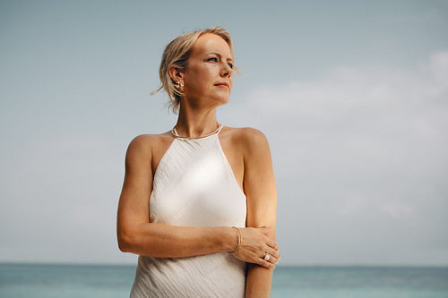 Elegant mature woman with gold jewelry posing by the ocean under a serene sky
