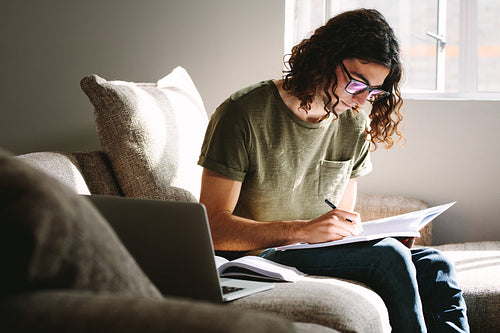 Student writing notes in a book sitting at home