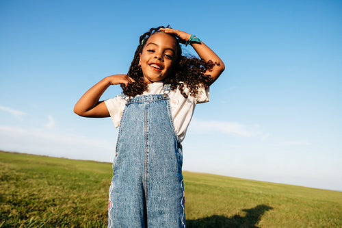 Bright young girl smiling in a wide open field under a blue sky