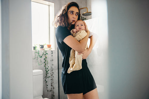 Mother brushes teeth while holding baby in bathroom