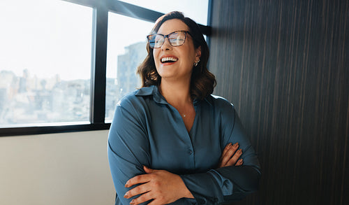 Joyful businesswoman in blue blouse laughing near office window