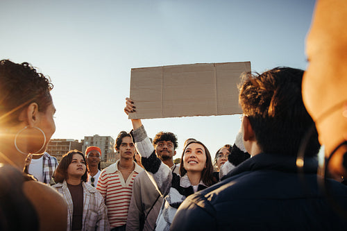 A young group gathers holding a blank sign outdoors at sunset