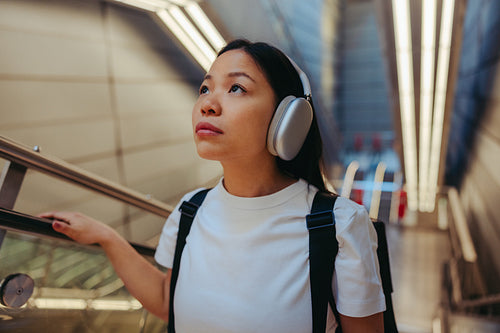 Young woman with headphones commuting on an escalator