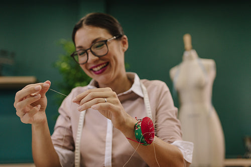Dressmaker threading the needle at fashion studio