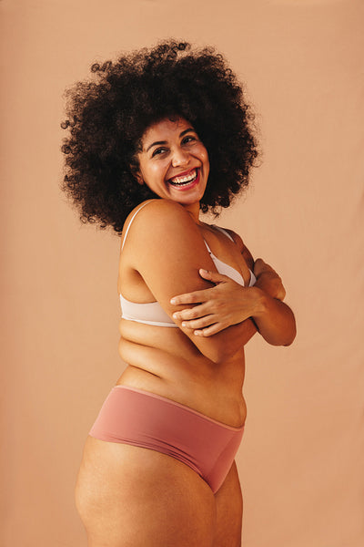 Smiling woman with an Afro hairstyle embracing her body in a studio