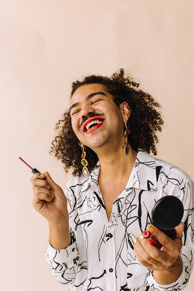 Smiling gay man applying make up in a studio