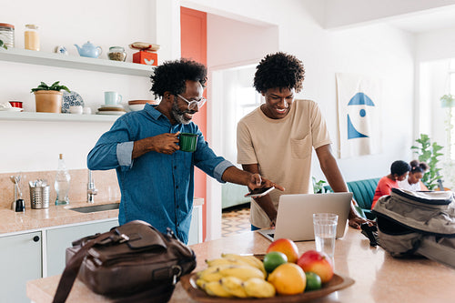 Mature man and his son use a laptop together during their morning routine at home