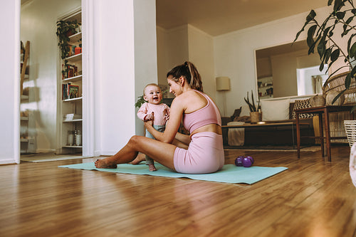 Young mother holding her adorable baby on an exercise mat