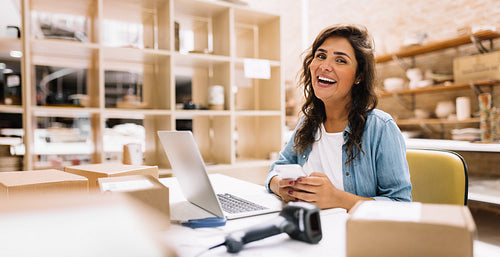 Happy female entrepreneur using a smartphone in a warehouse