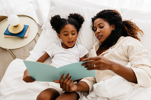 Mother and daughter reading a book together in bed