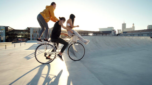 Playful friends riding a bicycle together in a skate park