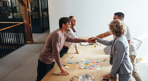 Professionals stacking hands together during a meeting in an office. Business team standing together in a boardroom