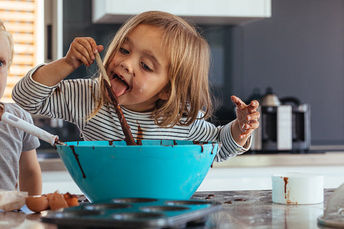 Girl licking chocolate cream while baking