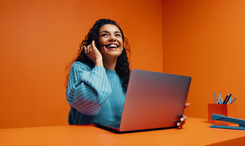 Freelance creative woman with long curly hair using a laptop and headset, smiling confidently