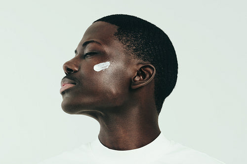 Young black man taking care of his skin with nourishing face cream