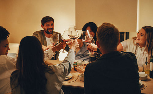 Friends toasting with wine and laughter during an intimate evening meal together