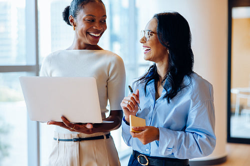 Two professional women discussing work while smiling in an office environment