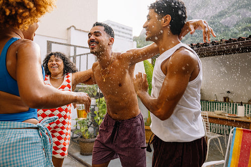 Brazilian friends laughing and splashing water during summer hose bath
