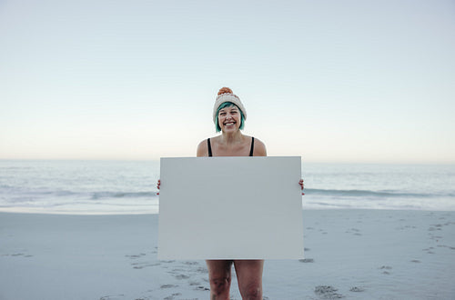 Self-confident winter bather holding a blan placard at the beach
