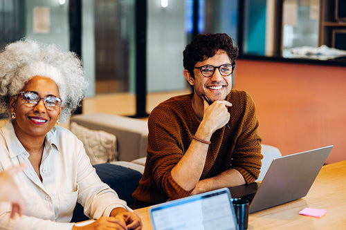 Two colleagues collaborate in a casual office space with laptops and notes