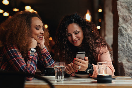 Young girls sitting at cafe and using phone