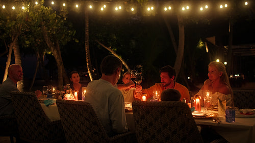Family vacationers share a joyful outdoor dinner at an island resort at night