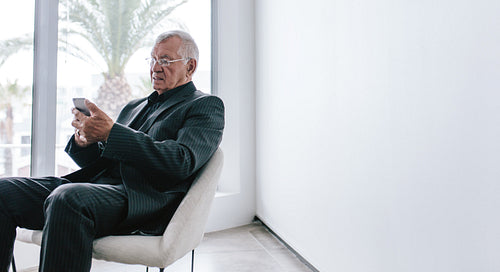 Senior businessman with mobile phone in office foyer