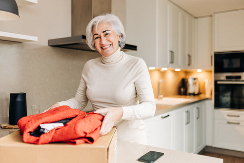 Cheerful senior woman unpacking her clothing delivery at home
