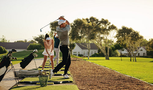 A couple enjoying a sunny day at the driving range, practicing their tee shots together