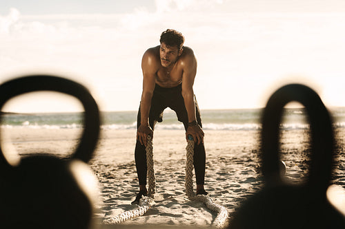 Man doing fitness training at the beach with battle ropes and kettlebells