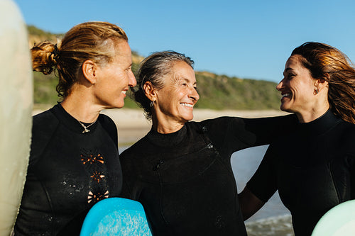 Three friends enjoying surfing together in wetsuits on a sunny beach