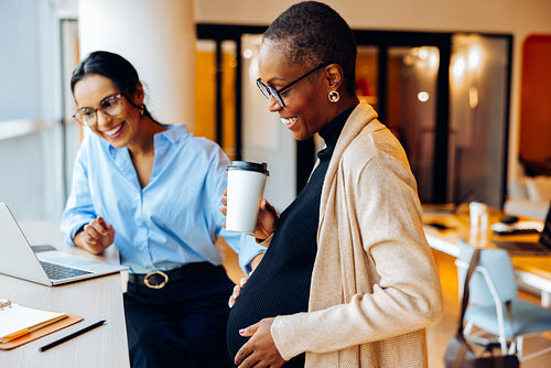 Two women discuss work while smiling in a bright office environment