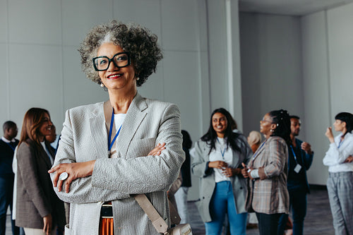 Confident mature female professional at a corporate business conference smiling with diverse colleagues in the background