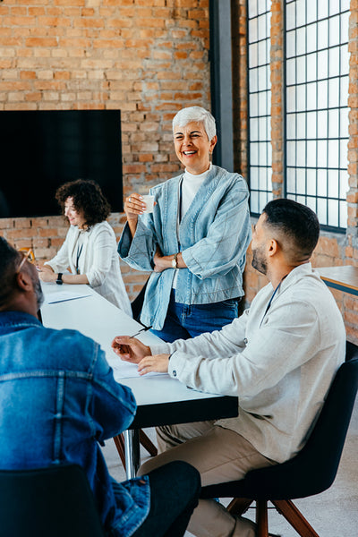 Relaxed mature business owner leading an informal meeting in a modern office setting with diverse team members enjoying a positive discussion in a bright space