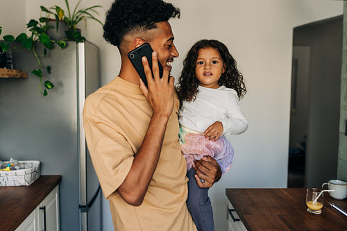 Happy young dad speaking on the phone while carrying his daughter