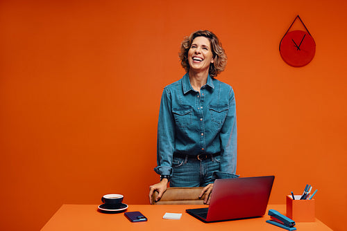 Digital marketer smiling confidently while working on laptop indoors in monochromatic orange set.