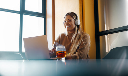 Smiling young woman using laptop and headphones at a bright workspace