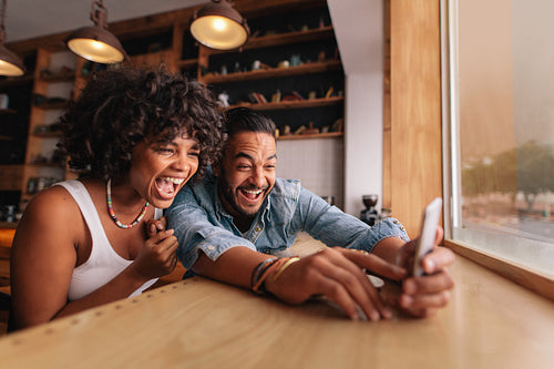 Young couple laughing and taking selfie in cafe