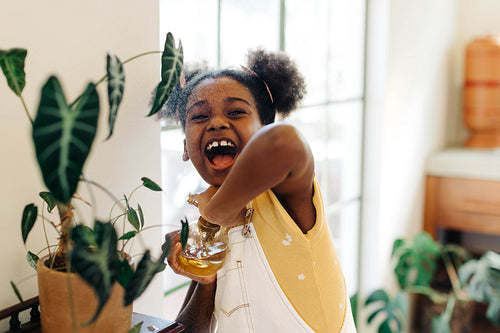 Excited girl spraying potted flowers in greenery-filled indoor garden