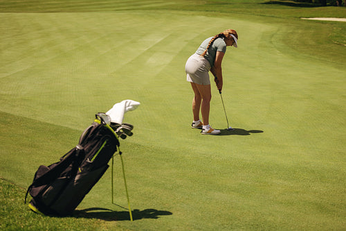 Focused woman takes a fairway shot on a sunny golf course with her golf bag beside her