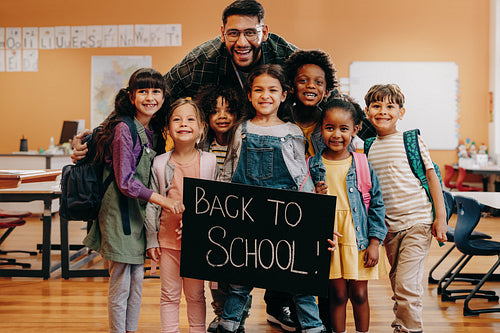 Primary school pupils excited to learn on first day of co-ed class. Teacher and kids hold a back to school sign
