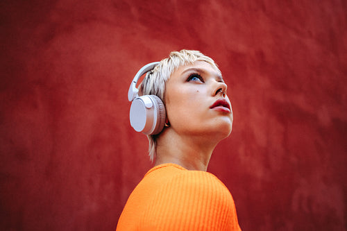 Woman wearing headphones gazes upward in thoughtful listening outdoors