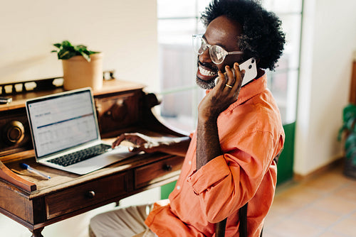 Cheerful Afro-Brazilian remote worker engaged in phone call at home office