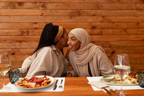 Young woman whispering to her friend in a restaurant