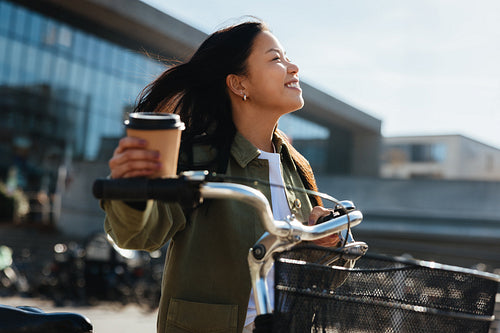 Woman with coffee walking with her bicycle on a sunny day in the city