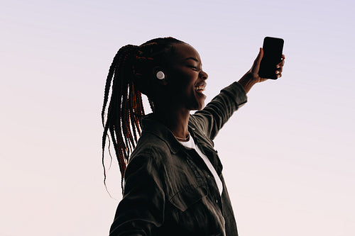 Happy woman taking selfie with earbuds and smartphone.