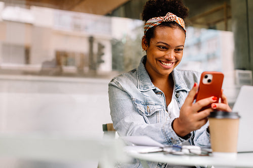 Cheerful woman using a phone during her coffee break at a coffee shop