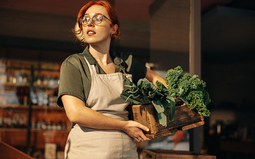 Female shop owner holding a box of fresh organic vegetables