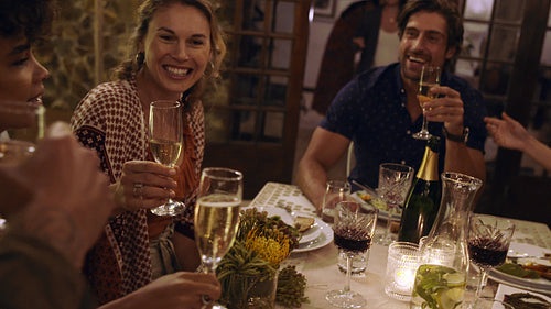 Multi-ethnic friends sitting at dinner table and having drinks at party